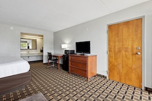 Habitación de hotel con cama, escritorio con computadora, televisor, cómoda y puerta.