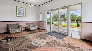 Un hall d’hôtel avec un tapis à motifs, deux canapés, une petite table, un tableau encadré au mur et une porte vitrée donnant sur l’extérieur.