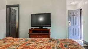 Una habitación con una cama, un televisor sobre un mueble de madera y dos puertas.