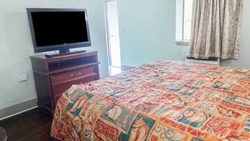 A bedroom with a bed, a TV on a wooden stand, a window with curtains, and a door.