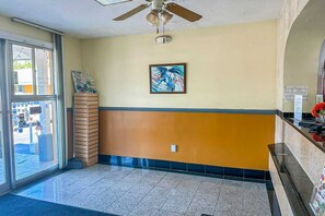 Un área de recepción con ventilador de techo, una obra de arte enmarcada, mostrador de recepción y ventana con vistas al exterior.