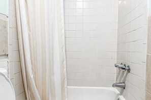 A bathroom with white tiled walls, a bathtub, and a shower curtain.