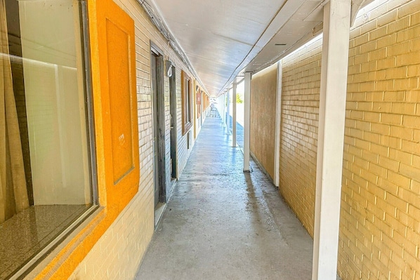 Un pasillo con piso de baldosas, paredes de ladrillo y puertas a la izquierda.