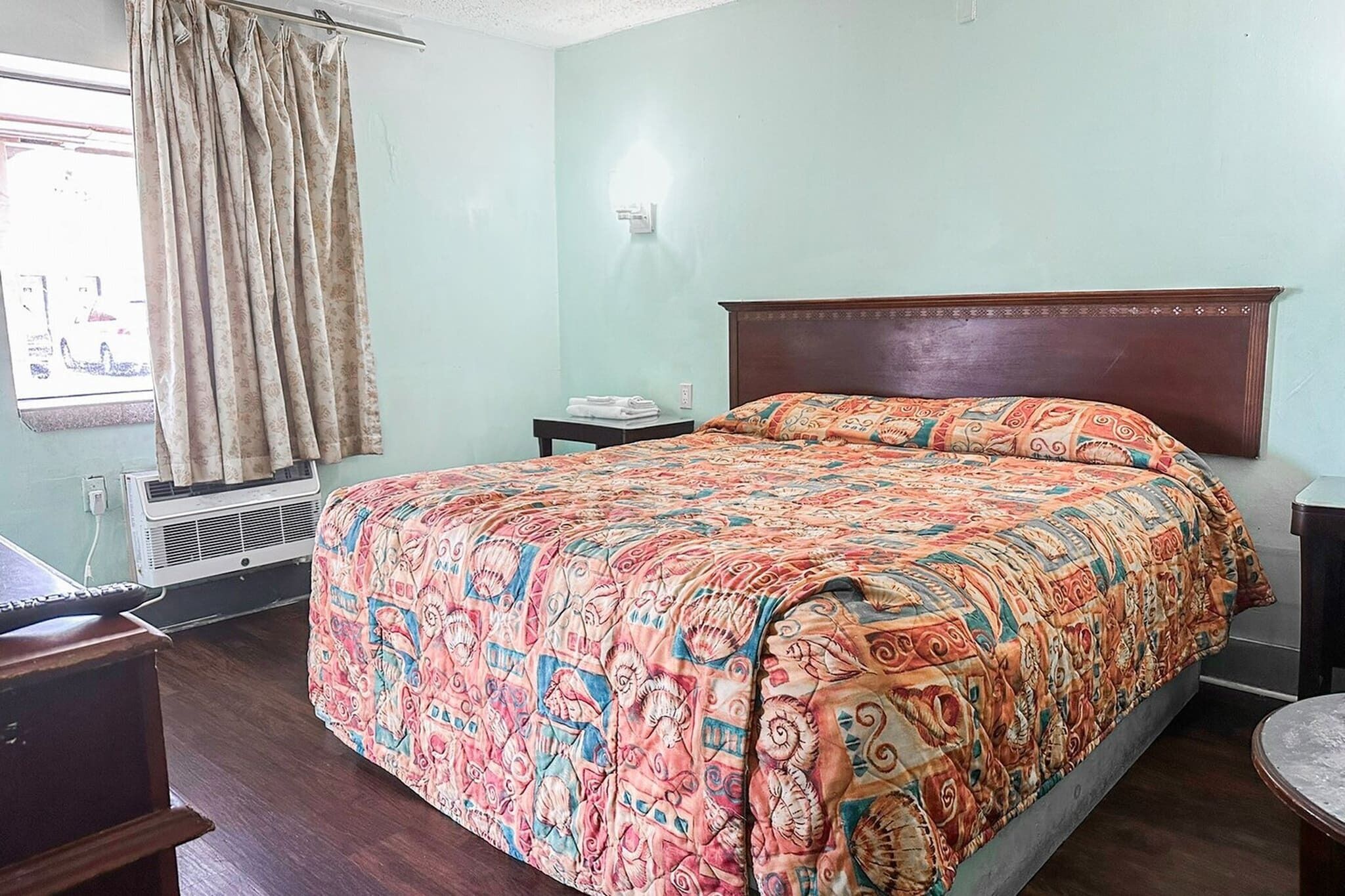 A bedroom with a bed, a nightstand, a chair, a window with curtains, and an air conditioning unit.