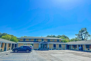 Un motel con edificio central y dos alas, un estacionamiento y un cielo azul despejado.