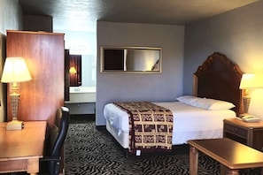 Ein Hotelzimmer mit einem Bett, Nachttischlampen, einem Spiegel, einem Holz-Kopfteil, einem Schreibtisch und einem gemusterten Teppich.