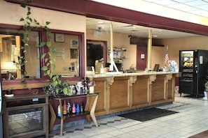 Un espace d’accueil comprenant un comptoir en bois, une machine à café, un réfrigérateur et une plante en pot.