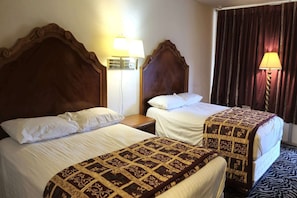 Twee bedden met houten hoofdborden, wit beddengoed en een bedsprei met een patroon.