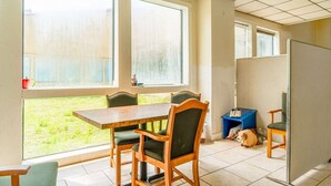 A room with a dining table, chairs, a small blue stool, a large window, and a view of a grassy area. - 2 Full Beds|Non-Smoking (Livingston)