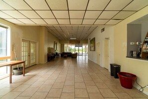 A spacious hallway with tiled flooring, a seating area with a sofa and chairs, a small table with a plant, and a trash bin.