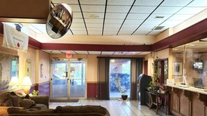 Un hall d’hôtel comprenant un comptoir d’accueil, un espace d’attente avec des canapés, un grand miroir et une entrée avec une porte en verre.