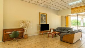 A living room with a piano, a television, a sofa, a coffee table, and a painting on the wall. - King Bed|Non-Smoking (Livingston)