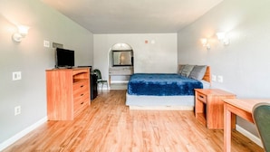 Ein Schlafzimmer mit einem Bett, einem Schreibtisch, einer Kommode, einem Fernseher und einem Spiegel.