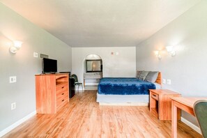 Un dormitorio con cama, escritorio, cómoda, televisor y espejo.