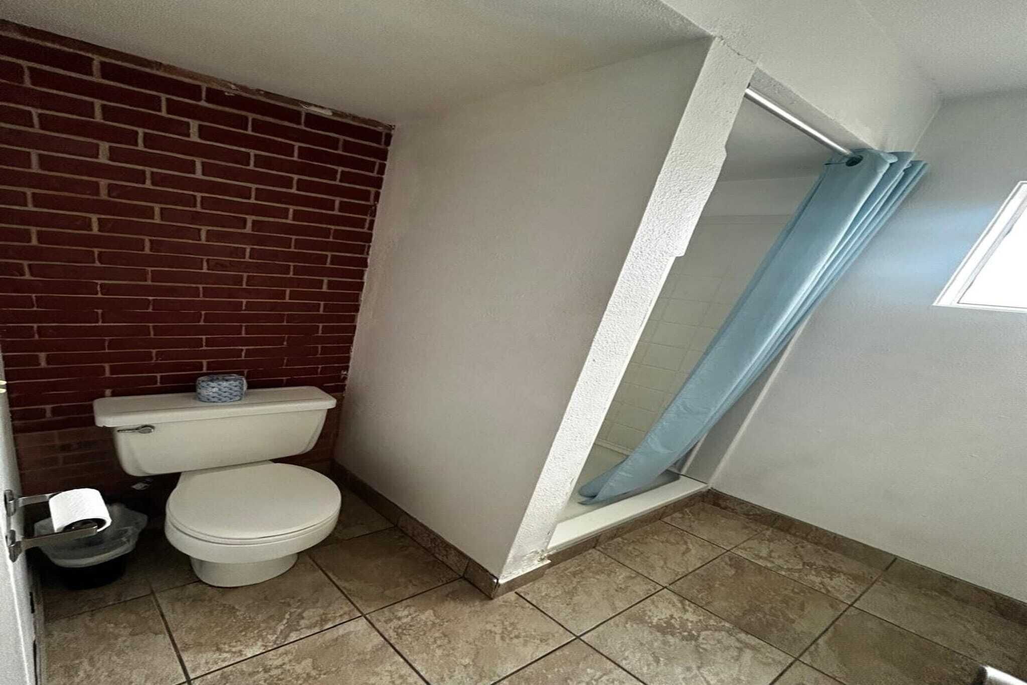Un baño con inodoro, un cubo de basura y cortina de ducha.