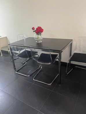 A conference table with four chairs, a vase with red flowers, and a clear plastic chair.