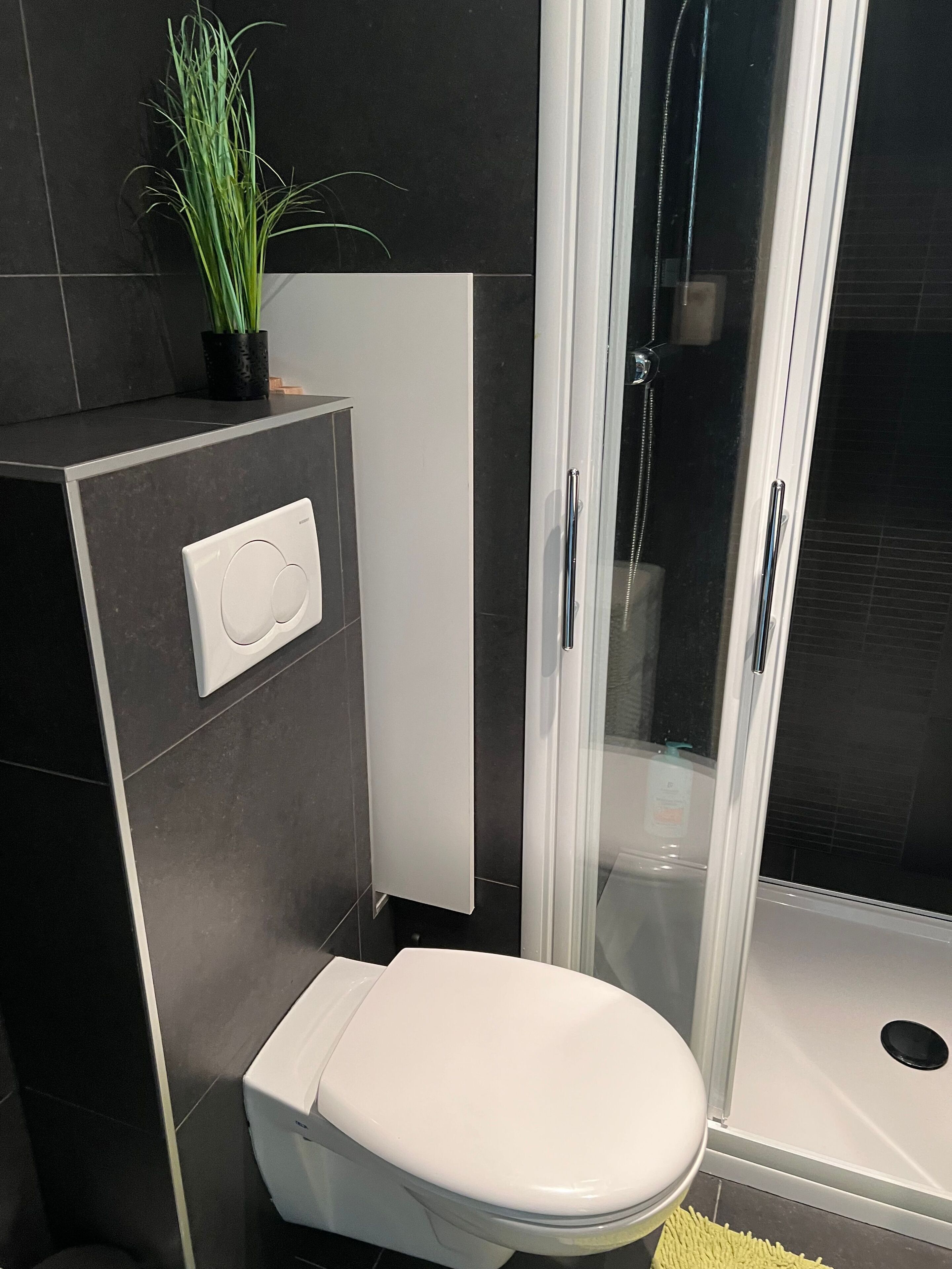 Ein modernes Badezimmer mit Toilette, Duschkabine und einer wandmontierten Bedienkonsole.