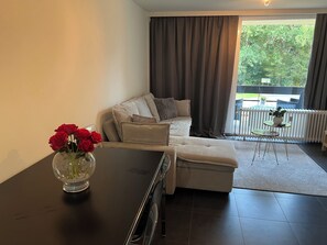 A living room with a sofa, a coffee table, and a vase with red flowers.