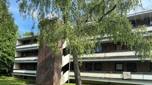 A multi-story building with a brick facade, a central tree, and a car parked in front. - Modern Apartment Near Aachen & Dreiländereck (Kelmis)