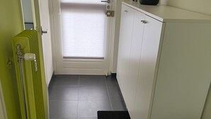 A narrow hallway with a radiator, a black mat, and a white cabinet with a red object on top. - Modern Apartment Near Aachen & Dreiländereck (Kelmis)