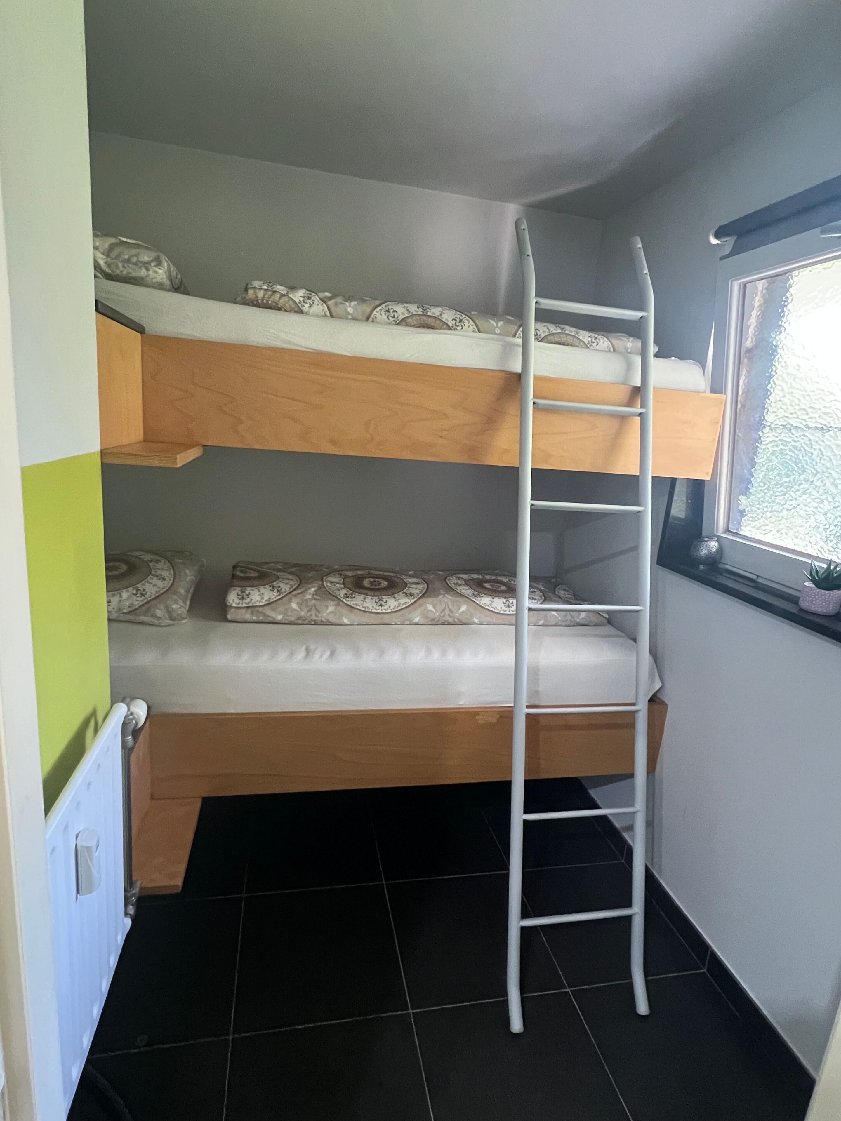Habitación con literas, una escalera, ventana y radiador.