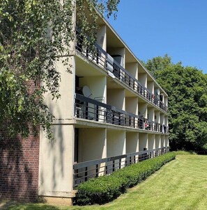 A multi-story building with balconies, a brick wall, and a well-maintained lawn.