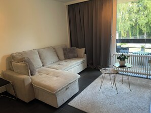 A living room with a sofa, a small table, and a view of the outdoors. - Modern Apartment Near Aachen & Dreiländereck (Kelmis)