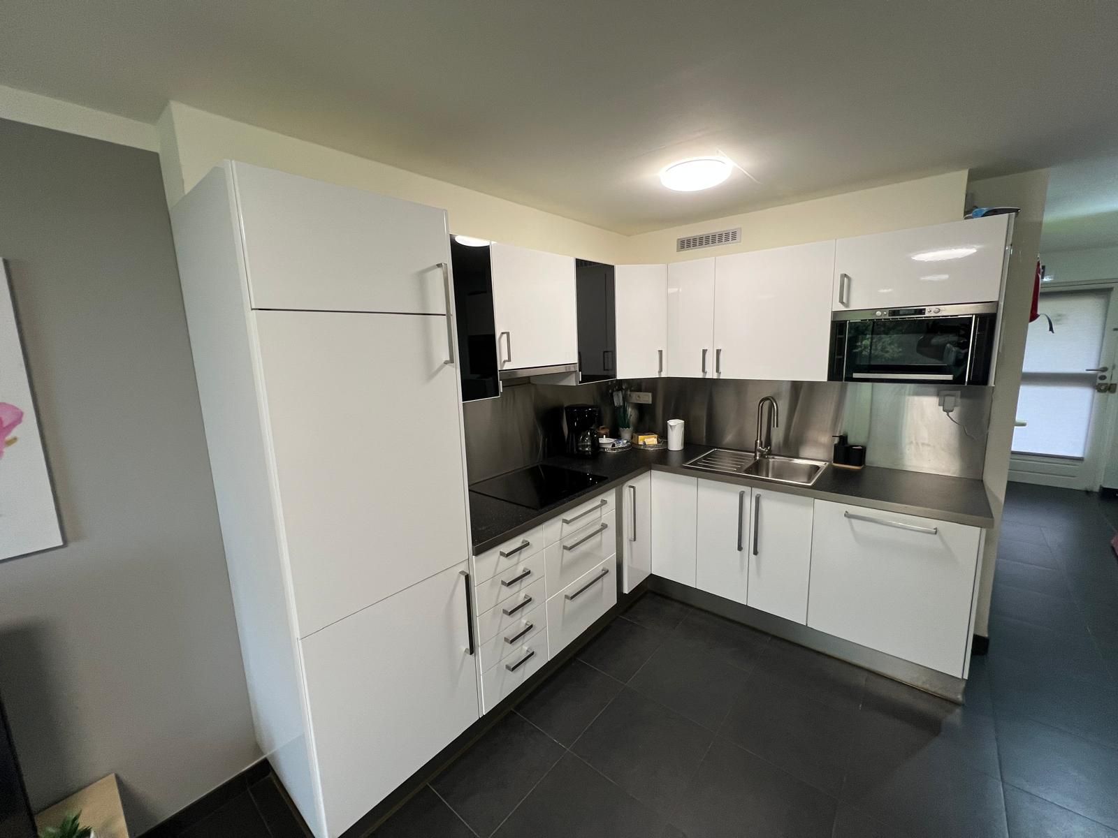 Een moderne keuken met witte kastjes, een zwart aanrecht, roestvrijstalen apparatuur en een inbouwspots.