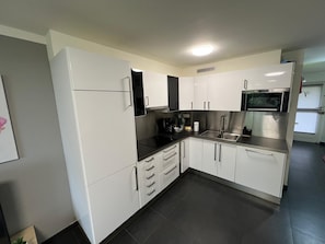 Una cocina moderna con gabinetes blancos, encimera negra, electrodomésticos de acero inoxidable y una luz empotrada en el techo.