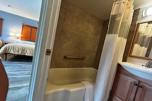 A bathroom with a bathtub, a shower curtain, a sink, and a mirror. - Queen Bed|Non-Smoking (Longview WA)