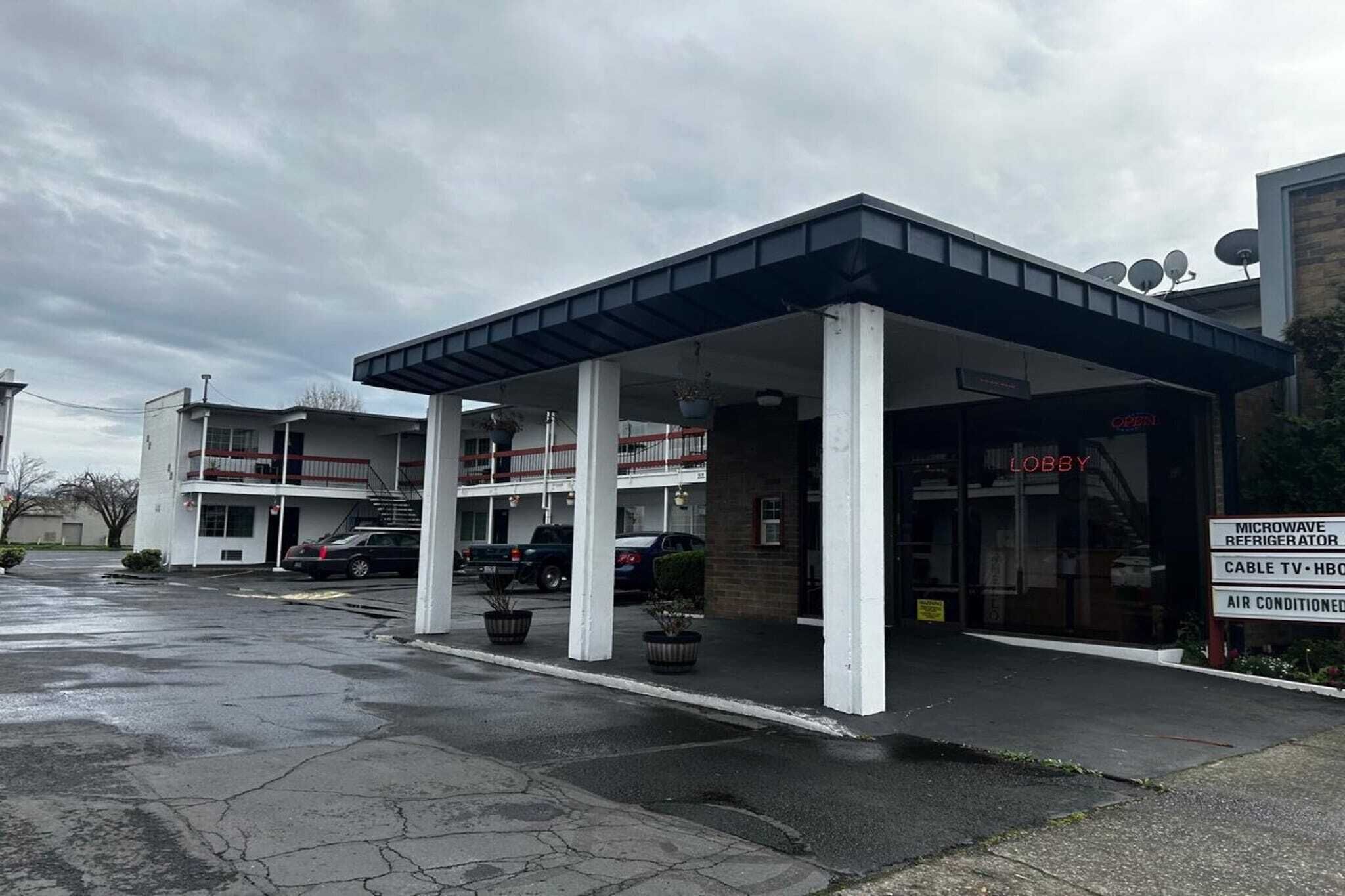 A building with a covered entrance, a visible lobby area, and a sign indicating amenities like a microwave refrigerator, cable TV, and air conditioning.