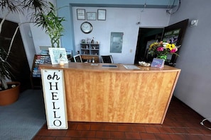 A reception desk with a 'hello' sign, a clock, certificates, a plant, and a flower arrangement. - Queen Bed|Non-Smoking (Longview WA)