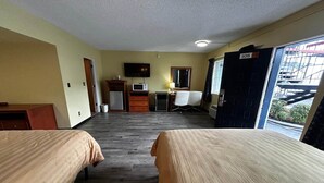 A hotel room with two beds, a TV, a desk with a computer, a microwave, and a view of a building outside.