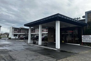 A building with a covered entrance, a visible lobby area, and a sign indicating amenities like a microwave refrigerator, cable TV, and air conditioning.