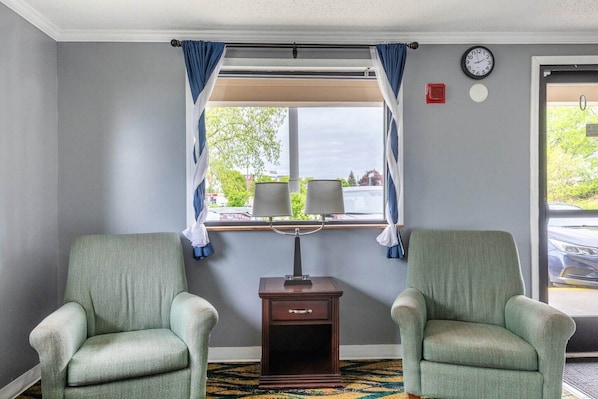 A room with two armchairs, a small table with a lamp, a clock on the wall, and a window with curtains.