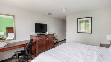 A hotel room with a bed, a desk with a chair, a television, a framed picture on the wall, and a mirror.