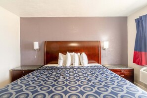 A hotel room with a bed, a nightstand, a lamp, and a wall-mounted heater. - Queen Bed|Non-Smoking (Lamesa TX)