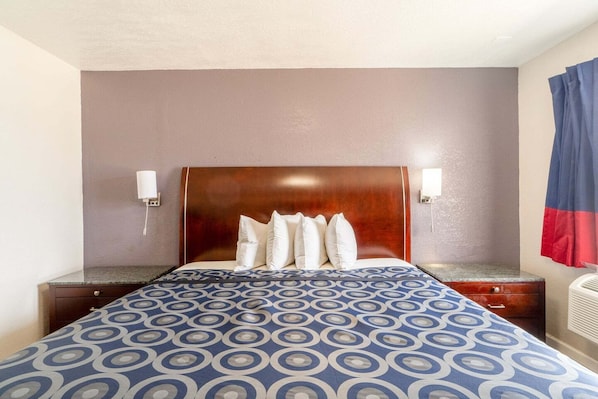 Una habitación de hotel con cama, mesita de noche, lámpara y un calentador fijado a la pared.