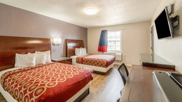 Een hotelkamer met twee bedden, een bureau, een televisie en een raam met gordijnen.