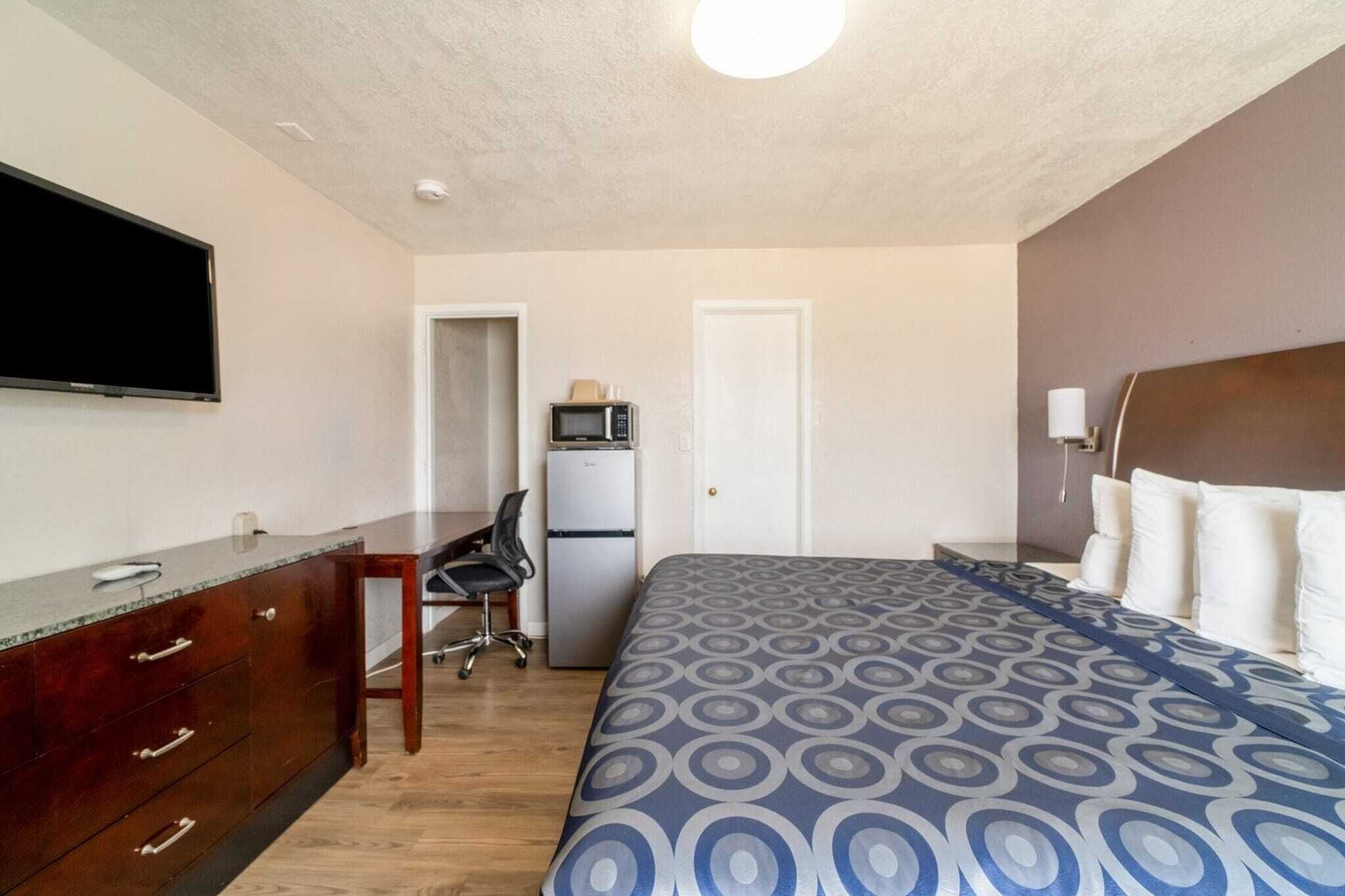A hotel room with a bed, a desk with a chair, a television, a microwave, and a refrigerator.