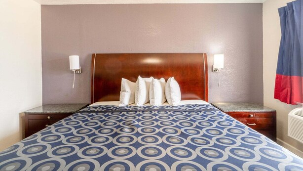 Una habitación de hotel con cama, mesita de noche, lámpara y un calentador fijado a la pared.