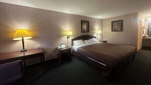 Ein Hotelzimmer mit einem Bett, zwei Nachttischlampen, einem Nachttisch mit Telefon und einem Schreibtisch mit Lampe.