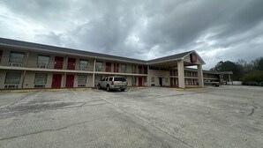 Ein Motel mit Parkplatz, überdachter Zufahrt und einem einstöckigen Gebäude mit zahlreichen Fenstern und Eingängen.