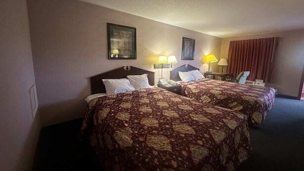 Habitación de hotel con dos camas, un escritorio, una silla y dos lámparas.