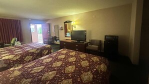 Ein Hotelzimmer mit zwei Betten, einem Fernseher, einem Schreibtisch und einem Sessel.