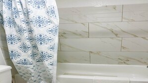 Ein Badezimmer mit Badewanne, Toilette und einer Duschvorhang mit geometrischem Muster.