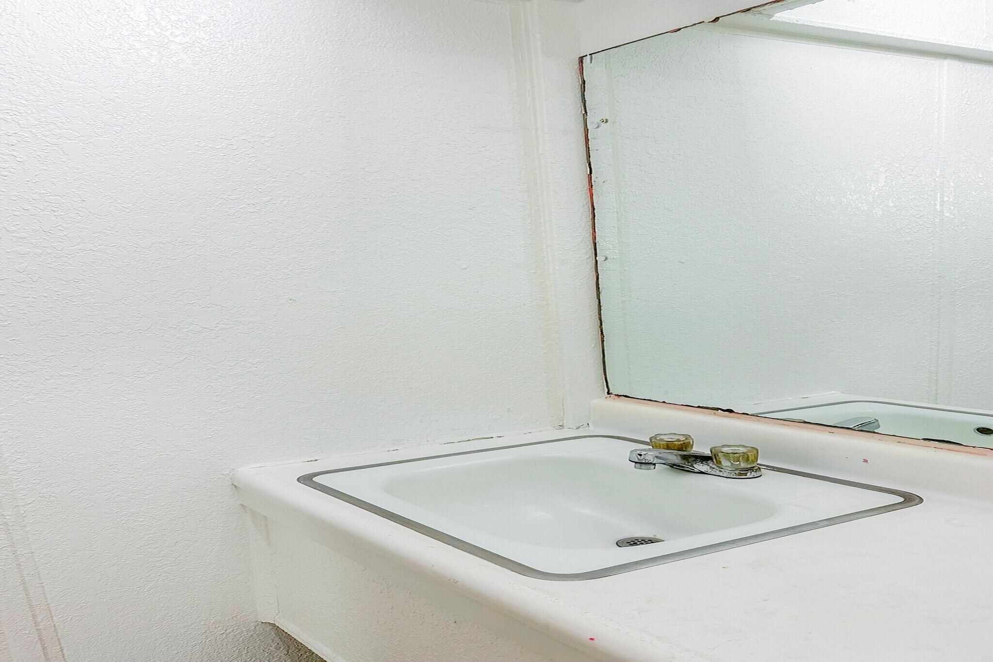 A bathroom with a white sink, a mirror, and a white wall.