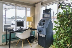 A room with a desk, computer, ATM, and a plant.