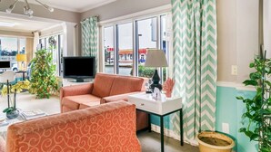 Un salon avec un canapé, un téléviseur, une table avec une lampe et une fenêtre avec des rideaux.