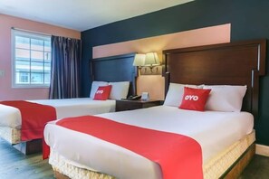 A hotel room with two beds, each with a red blanket and pillow, a nightstand with a lamp, and a window with curtains. - Myrtle Beach SC | 2 full bed (Myrtle Beach SC)